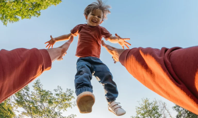 Smiling child being lifted into the air by a parent outdoors.